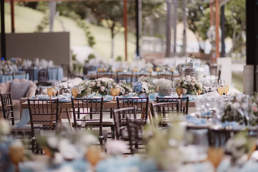 A hotel welcome desk dressed for a wedding party, stacked ivory welcome hampers tied with gold cord and a tray of marigold garlands, staff mid-task