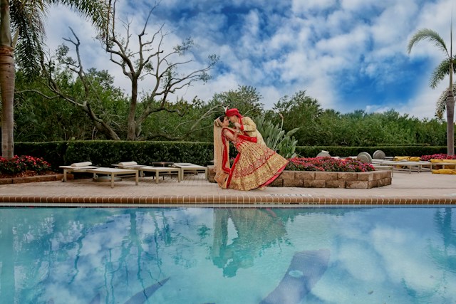 A photographer crouched at the edge of a pheras ceremony, fire and marigold garlands soft in the background